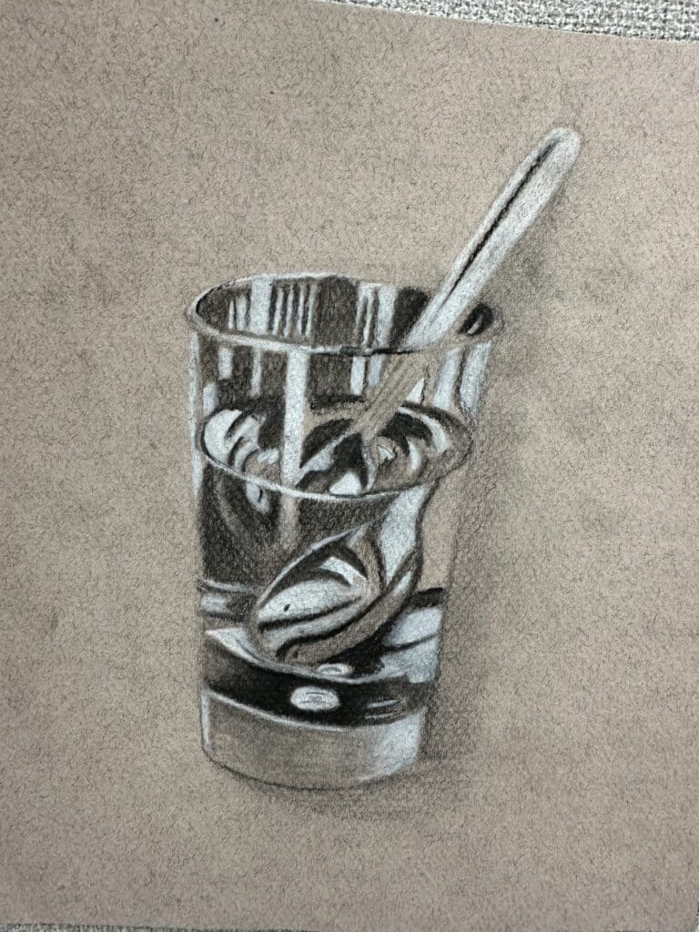 Easy charcoal still life drawing of a glass with black and white colored pencil on toned paper. Inspiration for  intermediate level high school art lesson.