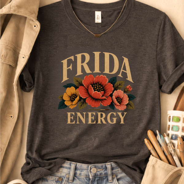 Gray art teacher t-shirt with a vintage floral design and the phrase “Frida Energy,” styled with art supplies nearby.